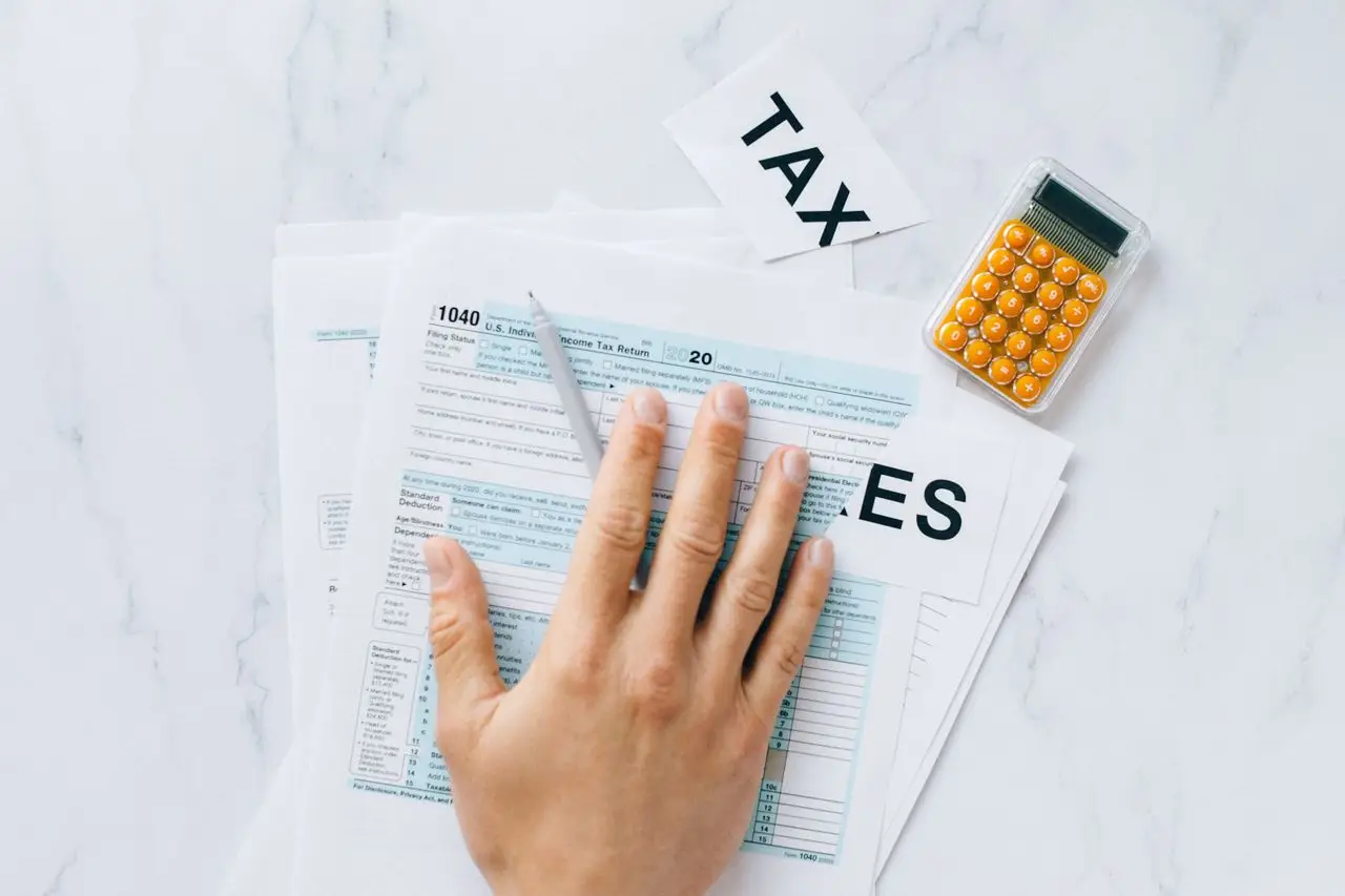 Close-up of a hand on tax form 1040 with a calculator on a desk.